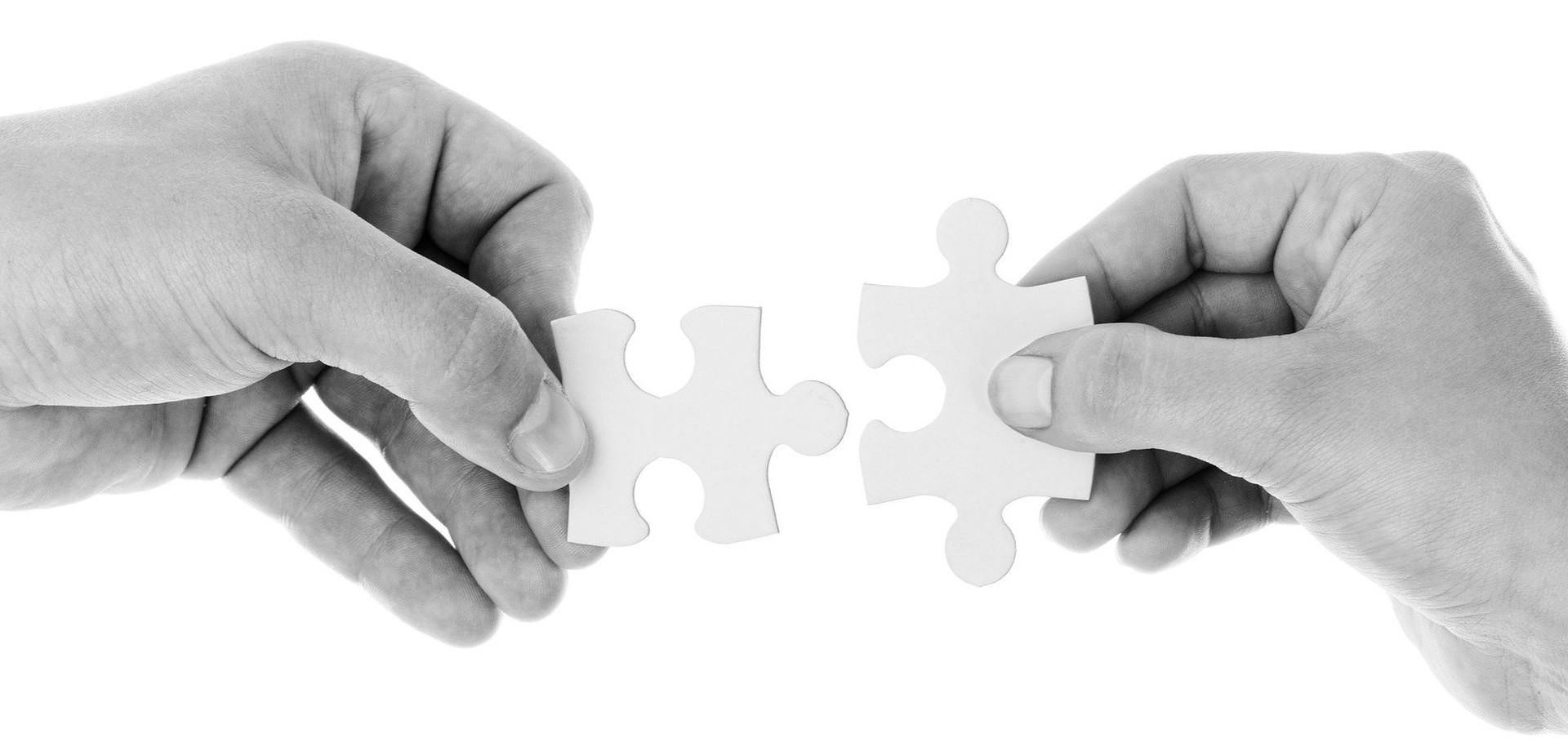 Zwei Hände, die zwei Puzzle-Teile zusammenführen.