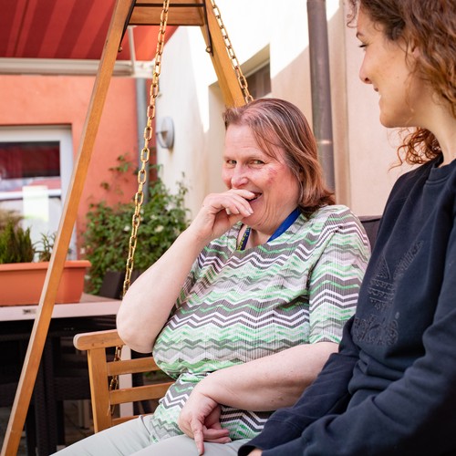 Eine leistungsberechtigte Person mit einer Assistenzkraft auf einer Gartenbank.